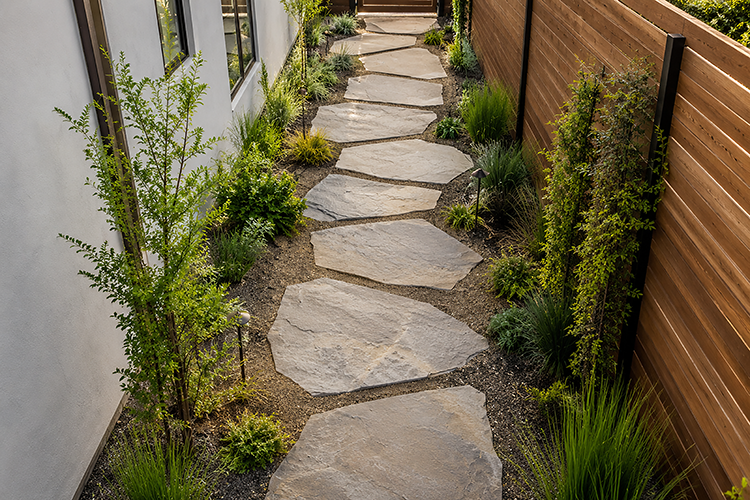 Natural flagstone stepping stones bordered by ornamental grasses and shrubs in a narrow side yard landscape design